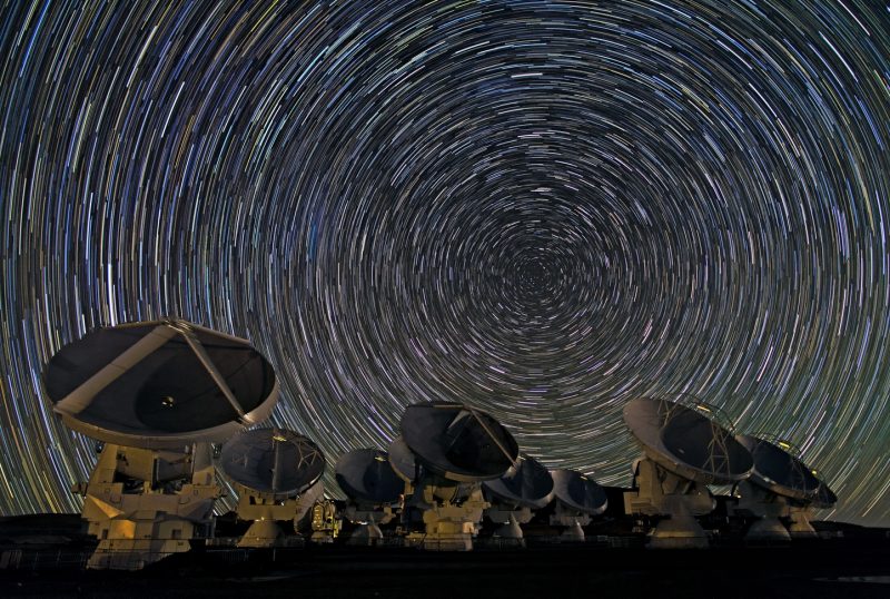 Very, very many short white concentric lines in the sky above 8 large radio telescope dishes.