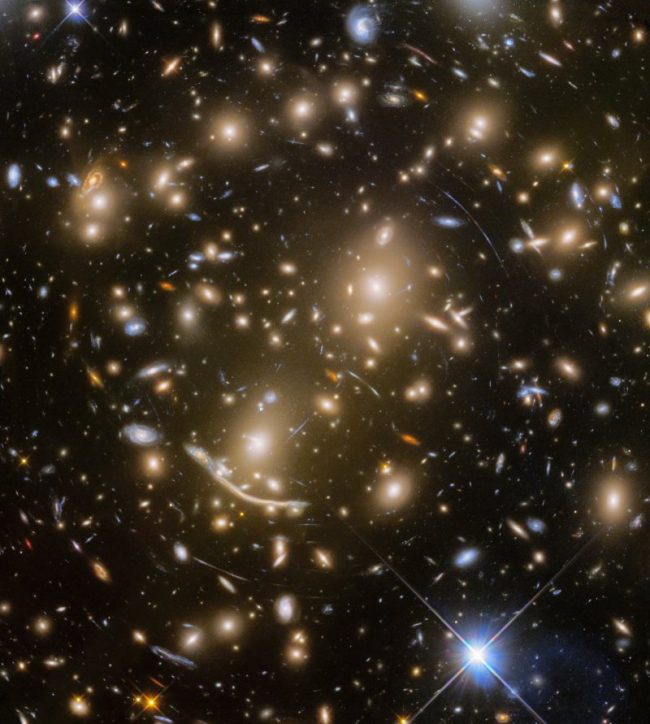 Black background with very many small golden galaxies and numerous arcs.