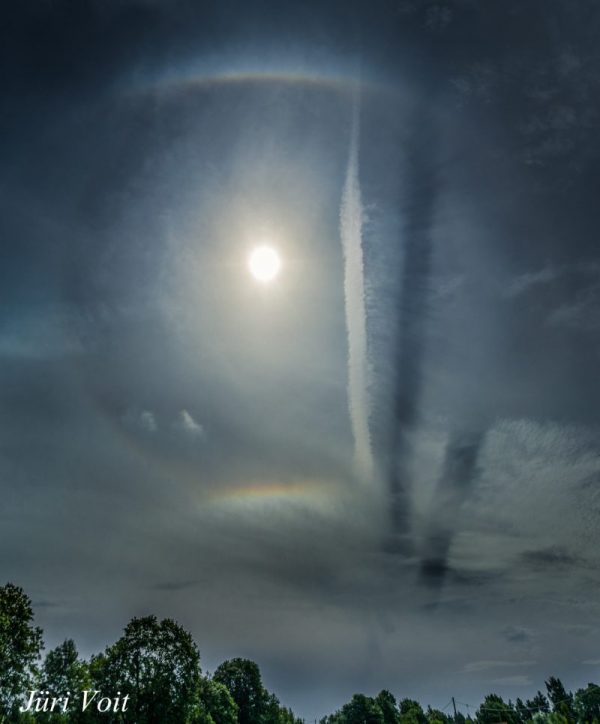 Bright light (sun) in top center, with a halo and a jet contrail with two shadows on its right side.