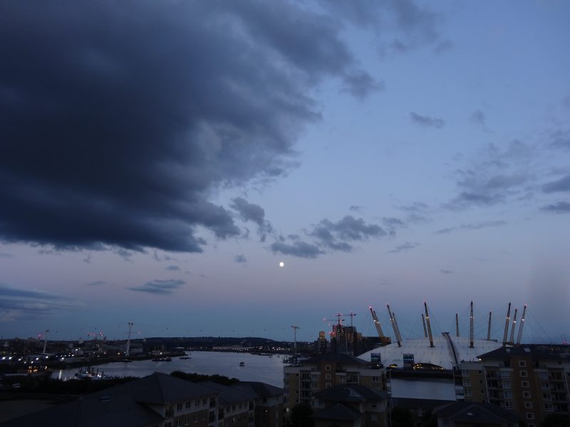 Tiny full moon in deep blue sky with dark band above horizon.