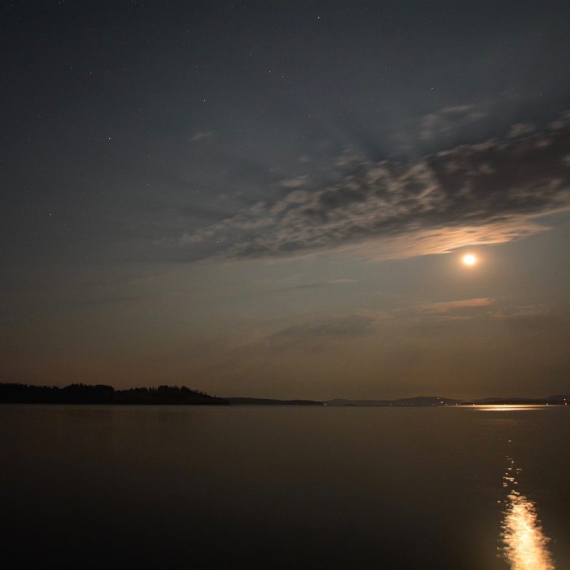 Orange moon with beams coming through clouds over a lake.