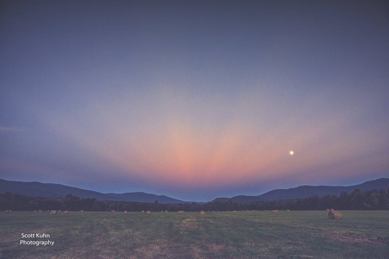 Faint pink rays converging to a point above low twilit hills.