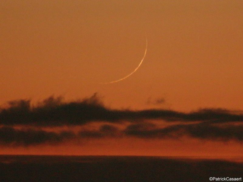 Very slender young moon in orange evening twilight.