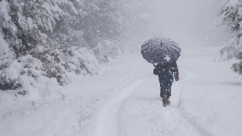 Lake-effect snow: A person in black trudges through deep snow with an umbrella.