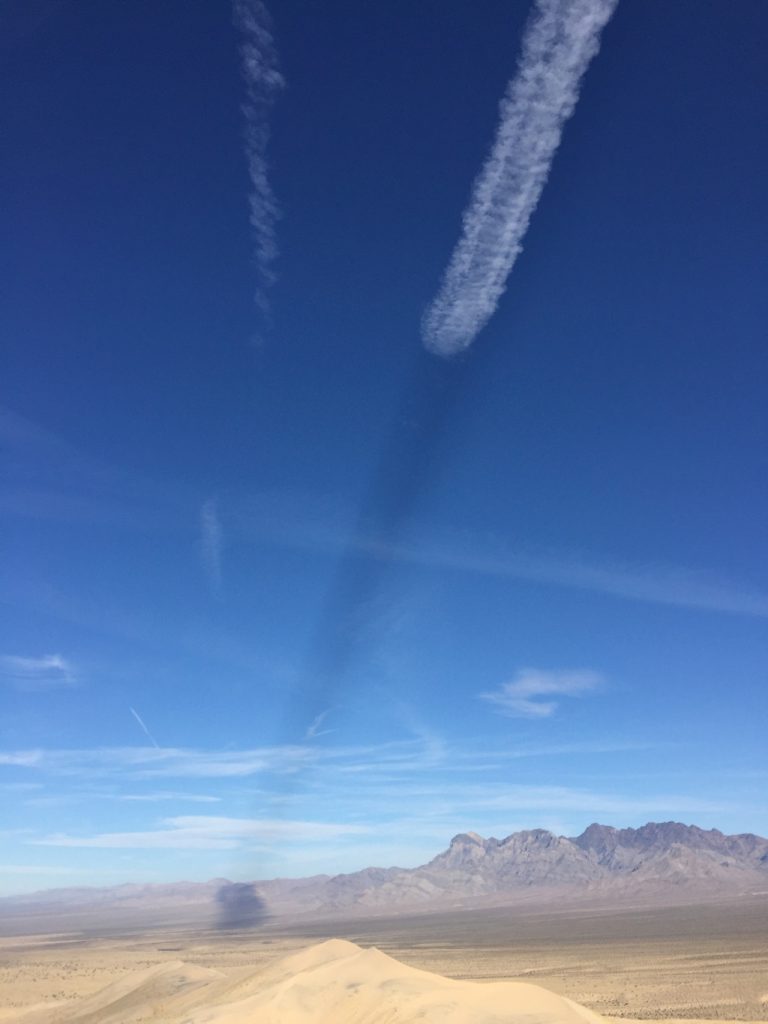 Landscape with mountains on the right horizon, blue sky and a jet contrail with a shadow. 