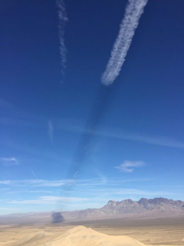 Landscape with mountains on the right horizon, blue sky and a jet contrail with a shadow.