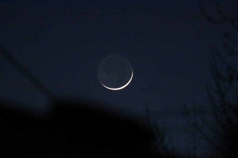 Thin glowing rescent moon with dark part of moon faintly visible in earthshine.