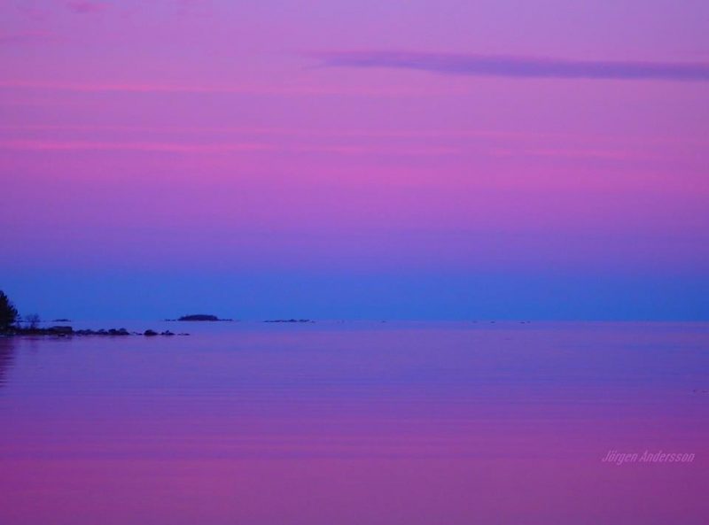 Purplish pink sky over blue band above horizon, reflected in calm sea.