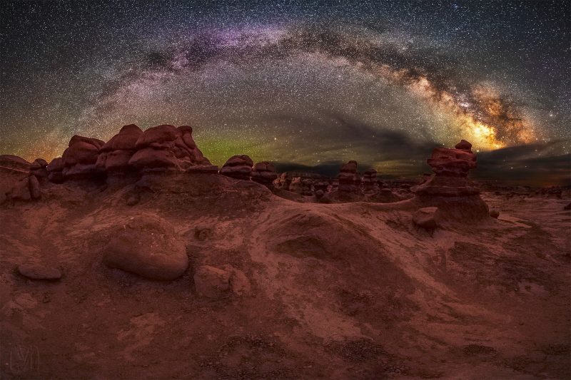 Starry arc of Milky Way, rising over a red rocky landscape.