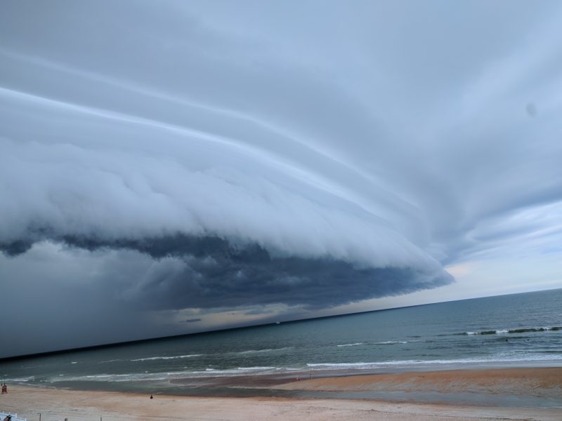 Bowed shelf cloud moving over a beach and ocean.