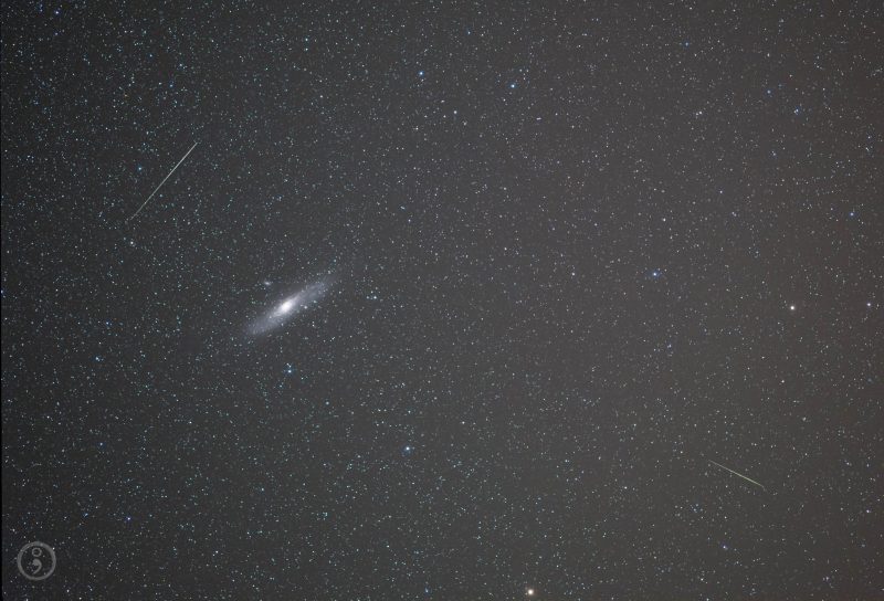 White oblong smudge with glowing spot in middle and 2 thin white meteor streaks in star field.