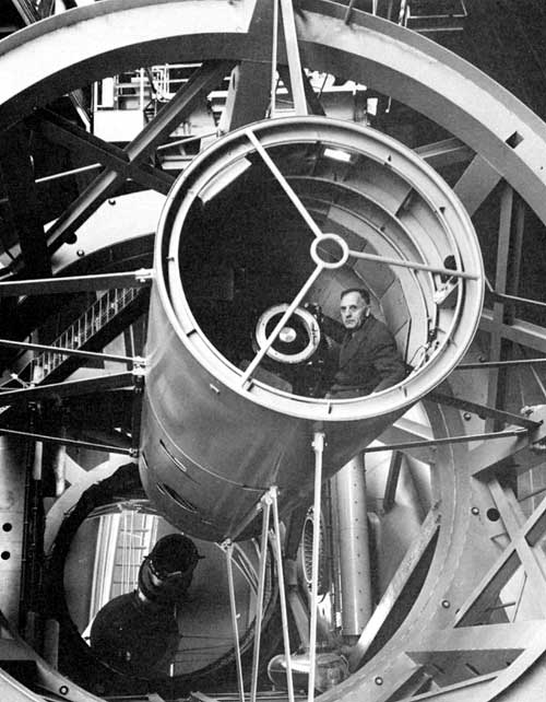 A person, Edwin Hubble, sitting inside a large optical telescope.