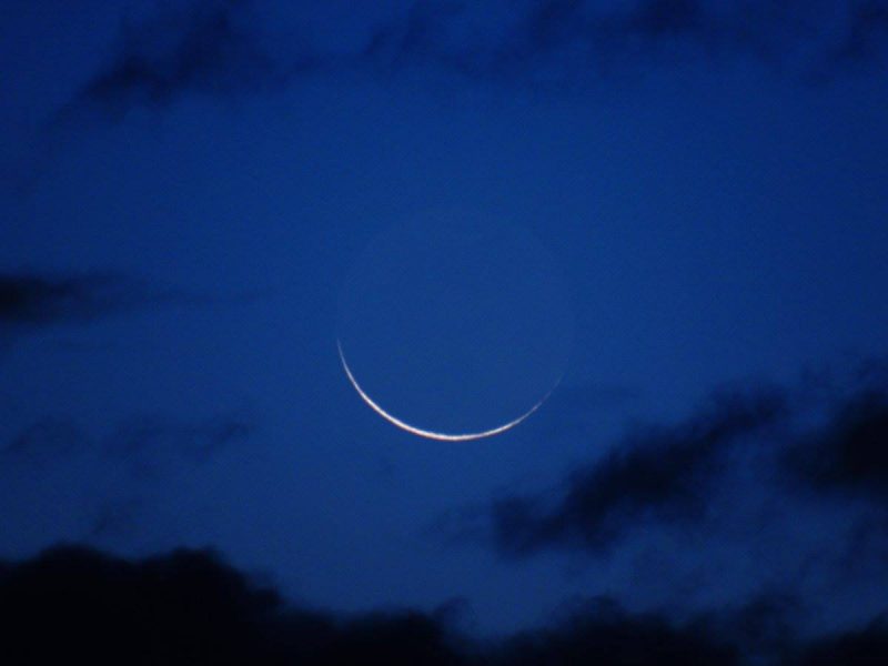Large blue circle with white crescent along one edge against nearly same color blue sky.