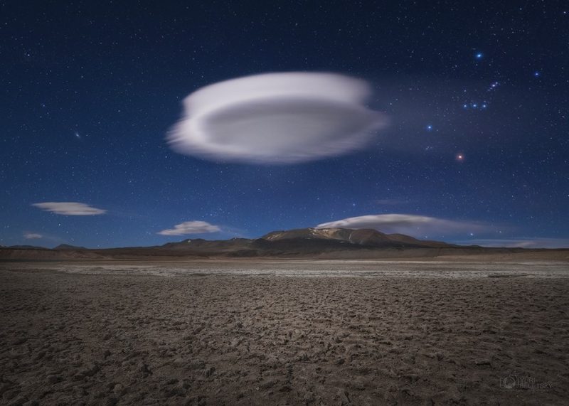 Saucer-shaped cloud hanging solitary above flat cracked brown desert.