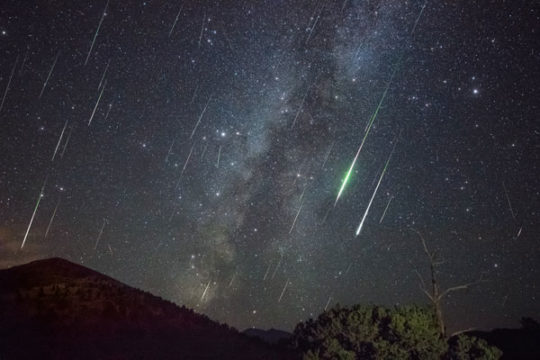 Milky Way in background, green Perseid meteors streaking downward in the sky.