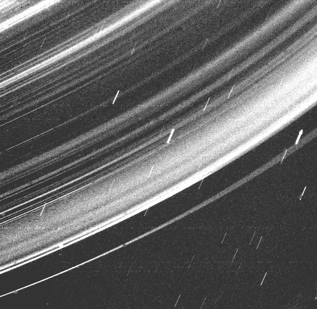 Section of many concentric rings of Uranus with short white streaks in foreground.