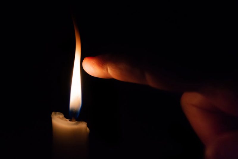 A finger close to a candle's flame.