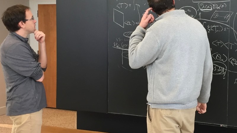 Two physicists looking at a blackboard covered with equations.