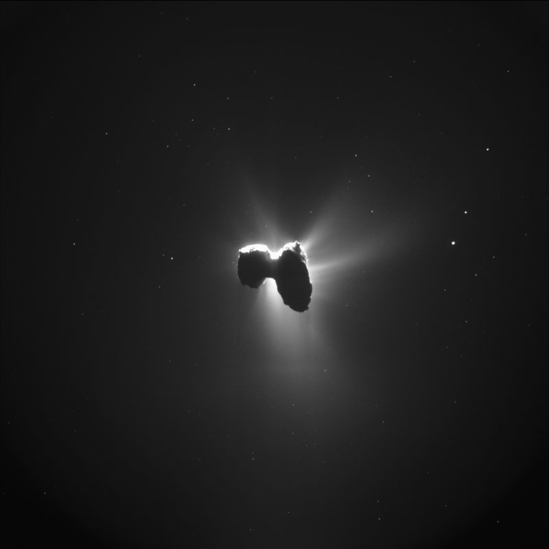 Famous Comet 67P: Backlit two-lobed object with straight streamers of glowing gas coming from it.