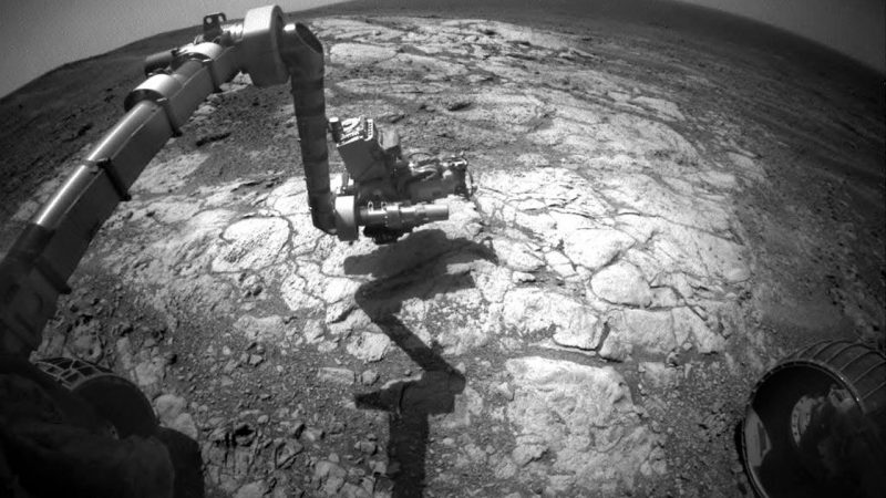 Jointed arm with tools over rocky surface, picture taken from main body of rover.