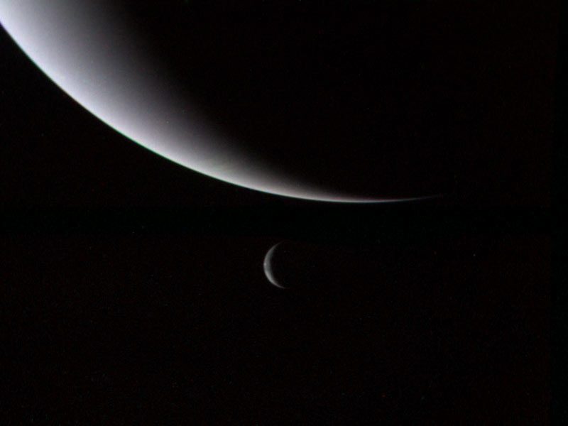 Crescent bluish large planet with crescent Triton below it.