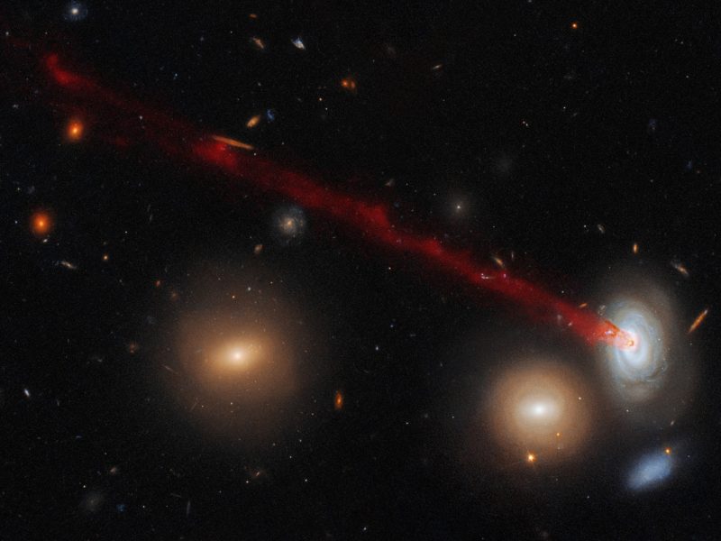 Four galaxies. Long red streak emerging from spiral galaxy.