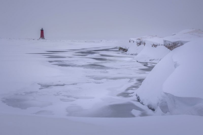 Frozen waves, lighthouse in background, icy cliffs to right.