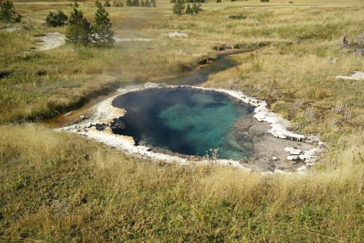 Pool of dark blue hot water surrounded by a white edge in a field.