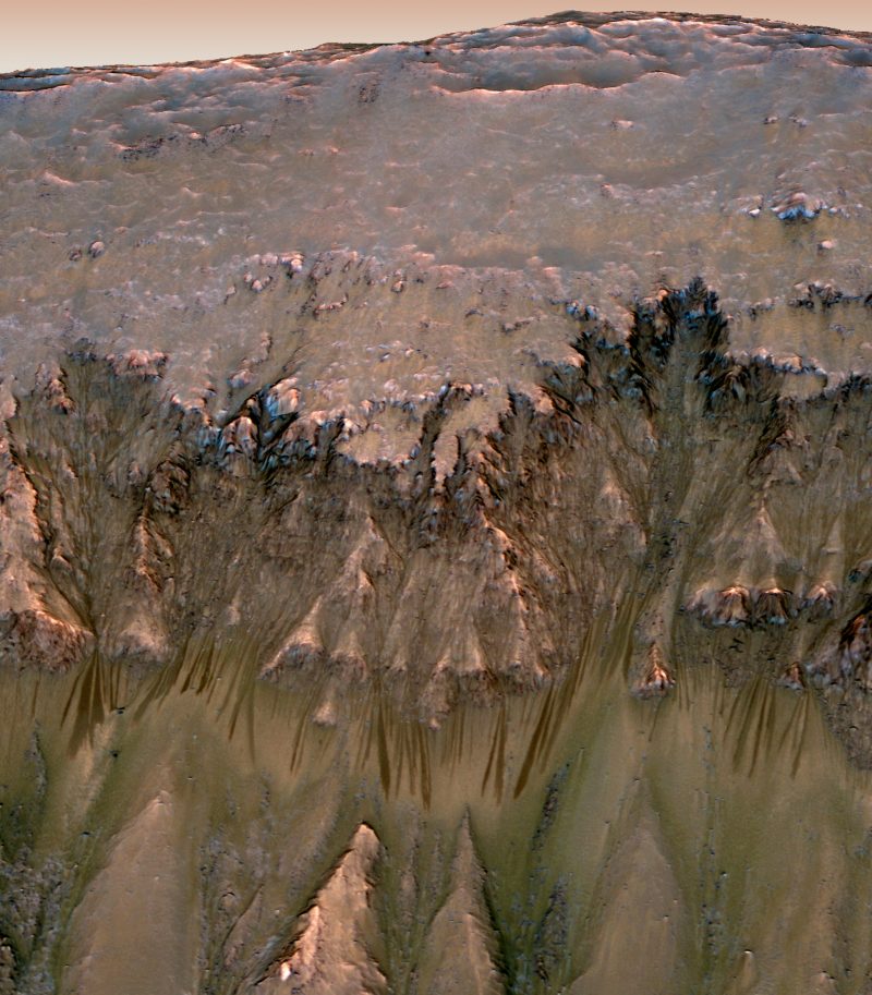 Long, thin dark streaks below triangular features on crater wall.