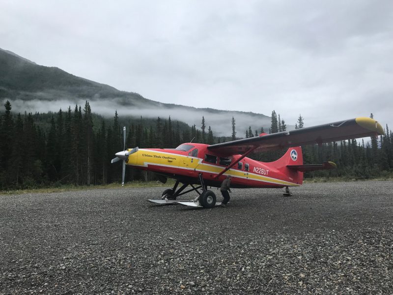 Red plane with four-blade propellor at nose and skis on wheels.