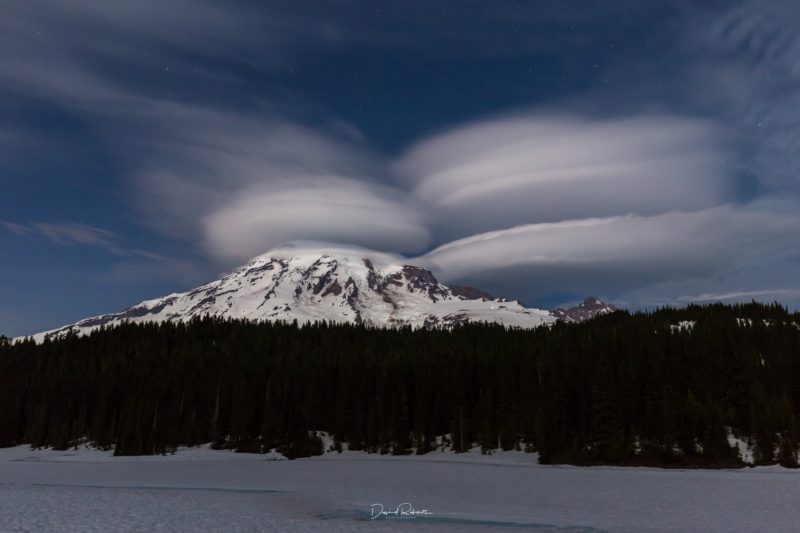 Several lenticular clouds above and beside snow-capped peak.