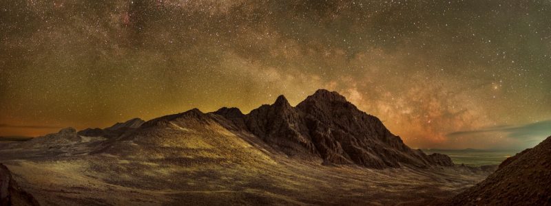 Milky Way over mountains and desert landscape with golden glow.