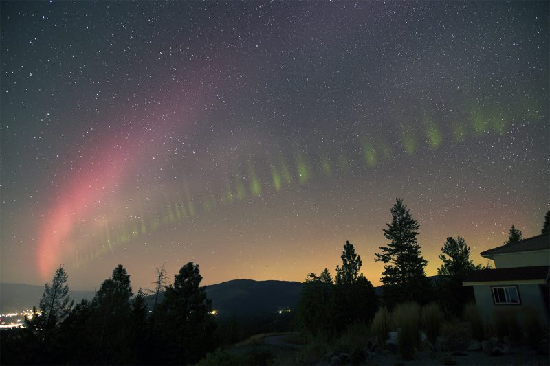 Arc of pink like next to green aurora divided into vertical lines.