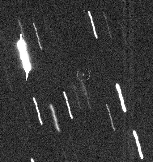 Long-exposure image of stars as streaks, with a tiny dot, the asteroid, circled in the center.