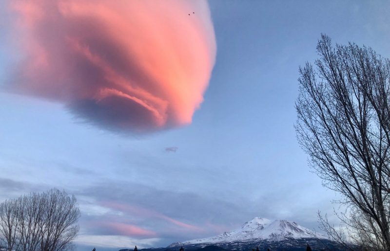 Saucer-shaped pink cloud, over a snow-covered, craggy mountain.