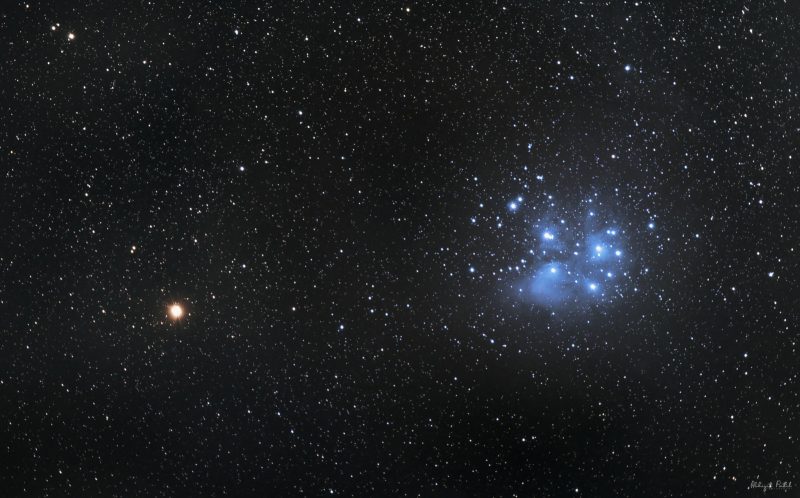 A red starlike point, Mars, next to a bluish dipper-shaped star cluster, the Pleiades.