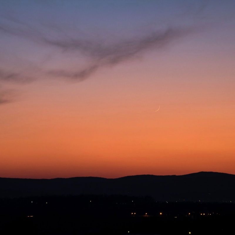 Thin young moon against an orange twilight sky.