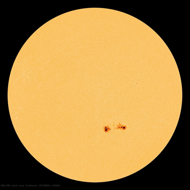 A big yellow ball- the sun - with two small sunspot groups in red.