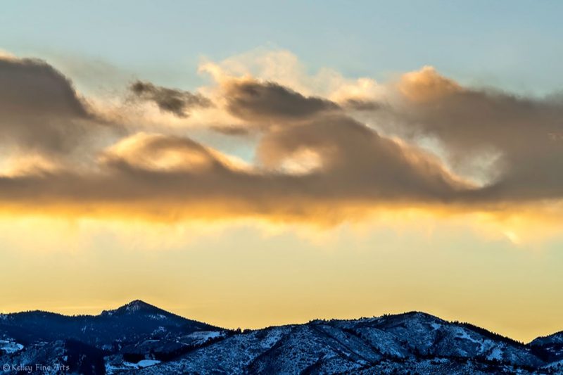 Big, fluffy, wave-shaped clouds at twilight, above a snowy mountain landscape.