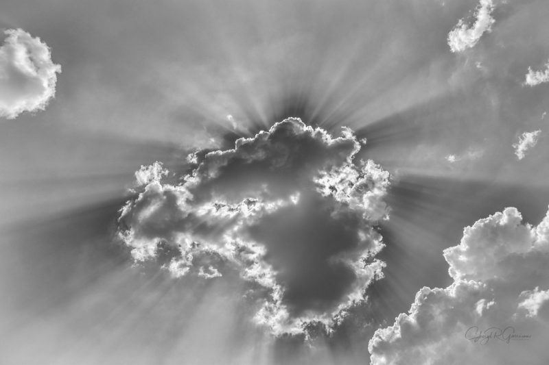 Black and white photo of a cloud in front of the sun with rays emendating
