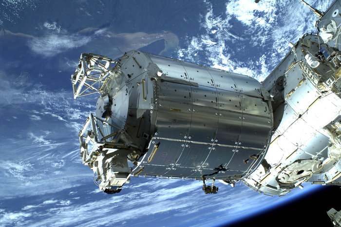 Shiny silver cylindrical spacecraft in front of blue planet Earth.