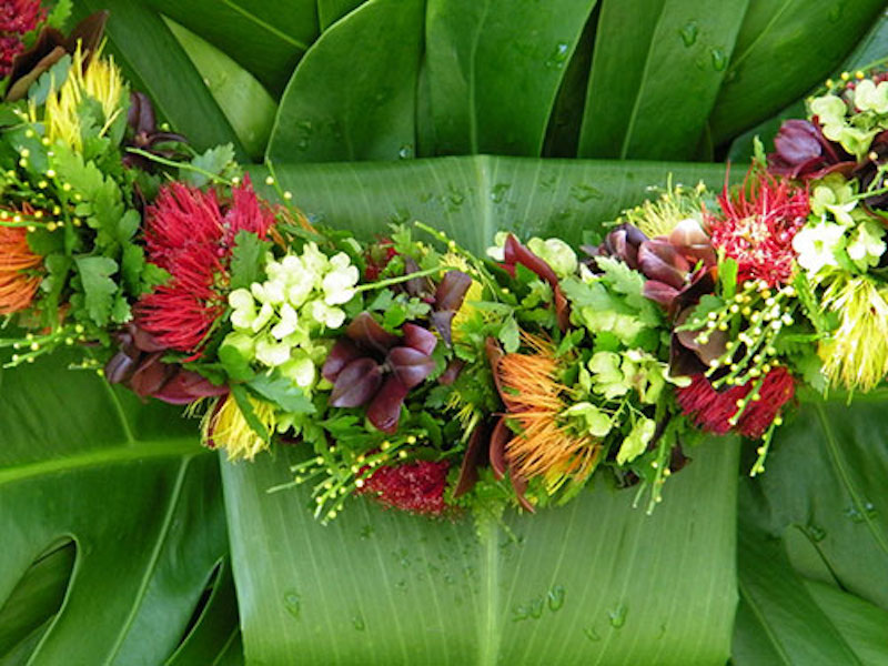 A garland of many flowers of different kinds against wide green leaves.