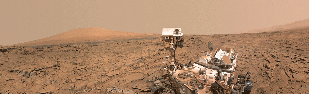 Rover on red Martian landscape with mountain in background.