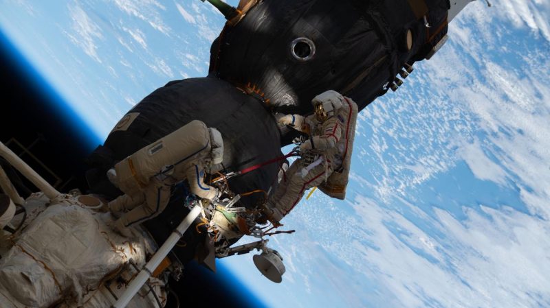 Astronauts in spacesuits outside a spacecraft with blue Earth in the background.