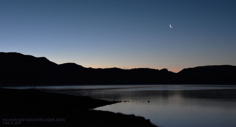 Moon and Venus at dawn over lake and silhouetted hills.