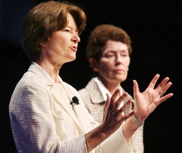 Two women standing next to each other with black background.