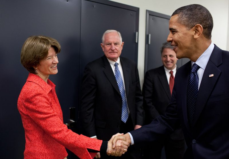 Woman in red jacket shakes hands with taller man in dark blue suit.