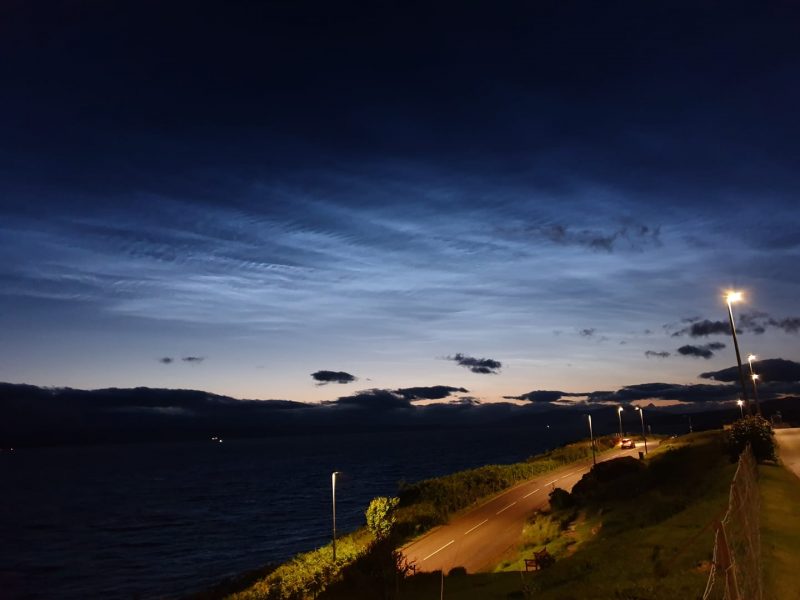 Blue shining clouds at night over perspective view of highway with street light to side.