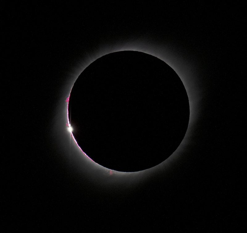 April 2023 solar eclipse: Black solid circle outlined with narrow fuzzy rim of light, with beads of light along one edge.