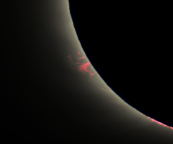 Close-up of one edge of the eclipsed sun, with a red prominence extending outward.